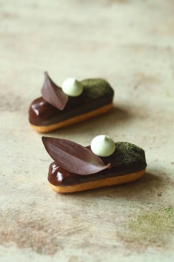 Geleneksel Fransız ekler Matcha Çay Pasta Kremi ile doldurulmuş ve çikolata jöleli, çikolata yapraklı ve kremalı kurabiyelerle süslenmiş, açık arkaplanda..