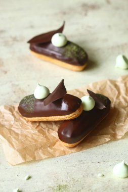 Geleneksel Fransız ekler Matcha Çay Pasta Kremi ile doldurulmuş ve çikolata jöleli, çikolata yapraklı ve kremalı kurabiyelerle süslenmiş, açık arkaplanda..