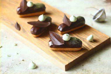 Geleneksel Fransız ekler Matcha Çay Pasta Kremi ile doldurulmuş ve çikolata jöleli, çikolata yapraklı ve kremalı kurabiyelerle süslenmiş, açık arkaplanda..