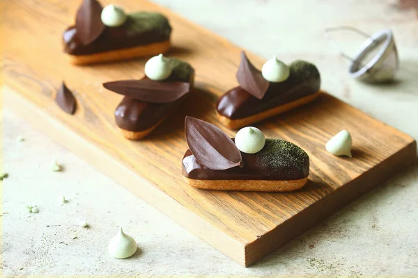 Geleneksel Fransız ekler Matcha Çay Pasta Kremi ile doldurulmuş ve çikolata jöleli, çikolata yapraklı ve kremalı kurabiyelerle süslenmiş, açık arkaplanda..