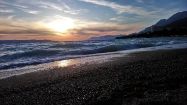 Hırvatistan. Makarska Riviera. Renkli günbatımının ve kumsaldan gökyüzünün muhteşem manzarası. Deniz kıyısı ve dalgalar. Kayalık plaj. Şehir parkı