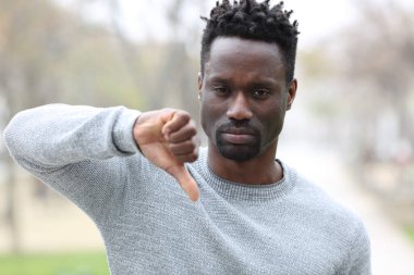 Siyahi bir adamın ön manzara portresi. Parkta dikilirken baş parmak işareti yapıyor.