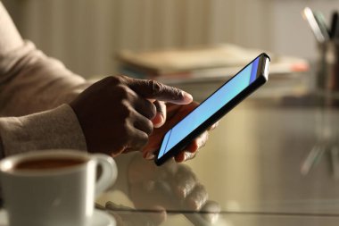 Gece veya iş yerinde cep telefonu kullanan siyahi bir adamın portresinin yan görüntüsü.