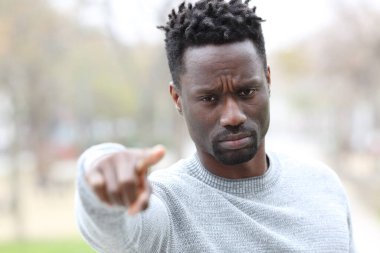 Siyahi, ciddi bir adamın ön manzara portresi. Parkta sana bakan kameraya bakıyor.