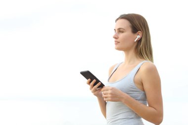 Kız kulaklık takıp müzik dinliyor. Beyaz arka planda duran akıllı bir telefon tutuyor.
