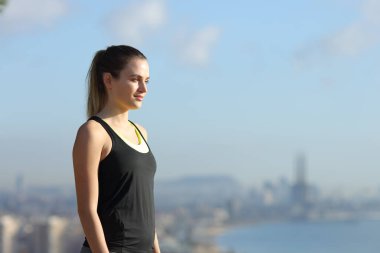 Güneşli bir günde şehrin arka planında dinlenen ve başka tarafa bakan mutlu bir koşucunun yan görüntüsü