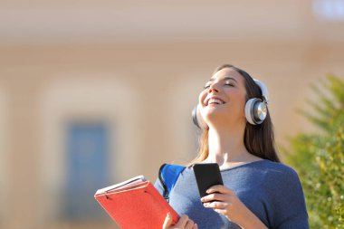Mutlu öğrenci temiz hava soluyor müzik dinliyor ve kampüste akıllı telefon tutuyor.