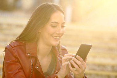 Mutlu kadın sıcak bir ışıkla sokakta oturan akıllı telefonu kullanıyor.
