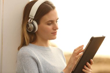 Gün batımında plajda tablet ve kulaklıkla ciddi bir gençlik e-öğrenimi.
