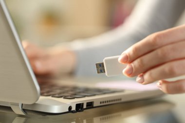 Kadın ellerinin USB flash belleği evdeki bir masada dizüstü bilgisayarın yanında tutması.