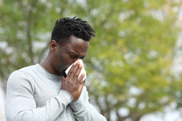 Allergic black man blowing on wipe in a park on spring season a sunny day
