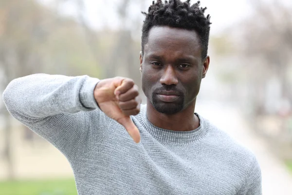 Siyahi bir adamın ön manzara portresi. Parkta dikilirken baş parmak işareti yapıyor.