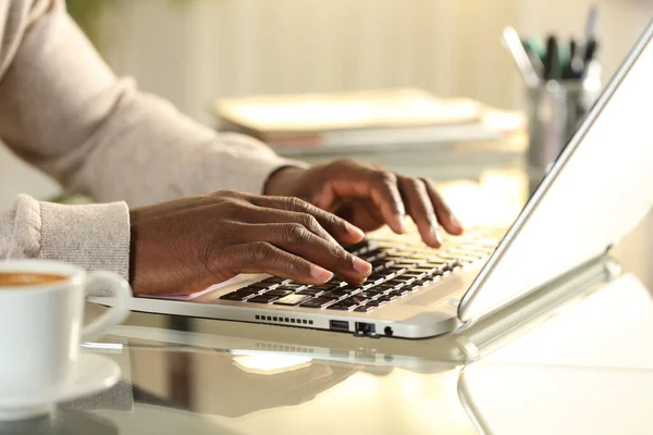 Close up of black man hands typing on a laptop on a desk at home