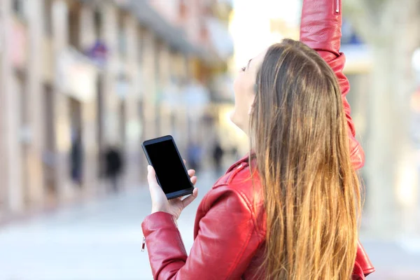 Arkaya bakan heyecanlı bir kız elinde telefonla sokakta boş bir ekran gösteriyor.
