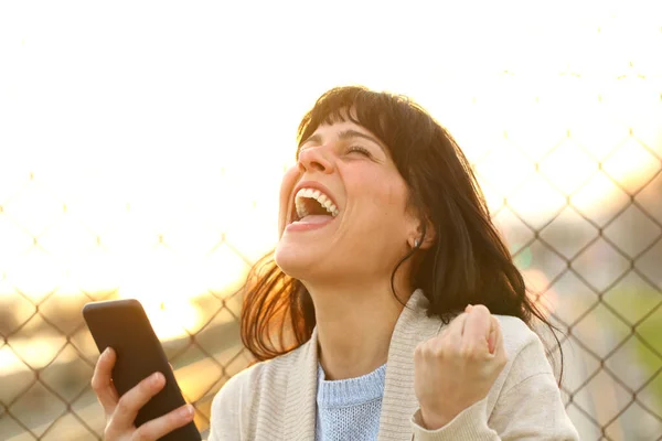 携帯電話を持って興奮した女性は日没時に路上で良いニュースを祝う — ストック写真