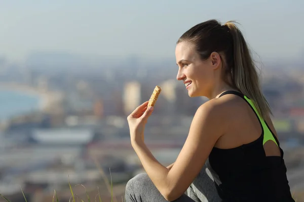 快乐跑步的女人在城郊运动后坐在室外吃能量棒 — 图库照片