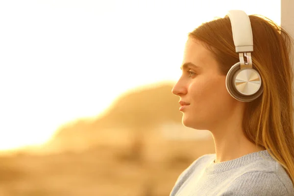 日落时戴耳机听音乐的妇女的简况 — 图库照片