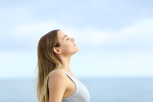 Profile of relaxed girl breathing deeply fresh air on the beach with a blue sky in the background
