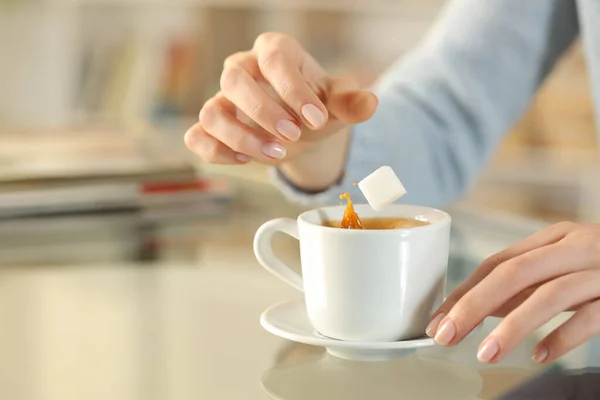 靠近一个女人 手把糖立方体扔在家里桌上的咖啡杯上 — 图库照片