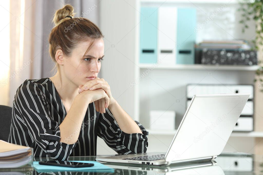 Confused entrepreneur woman looking at laptop sitting on a desk at the office