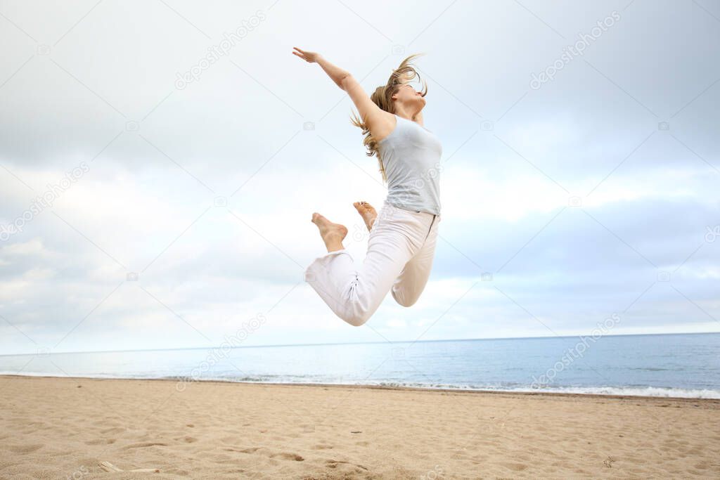 Full body portrait of an excited happy woman jumping on the beach