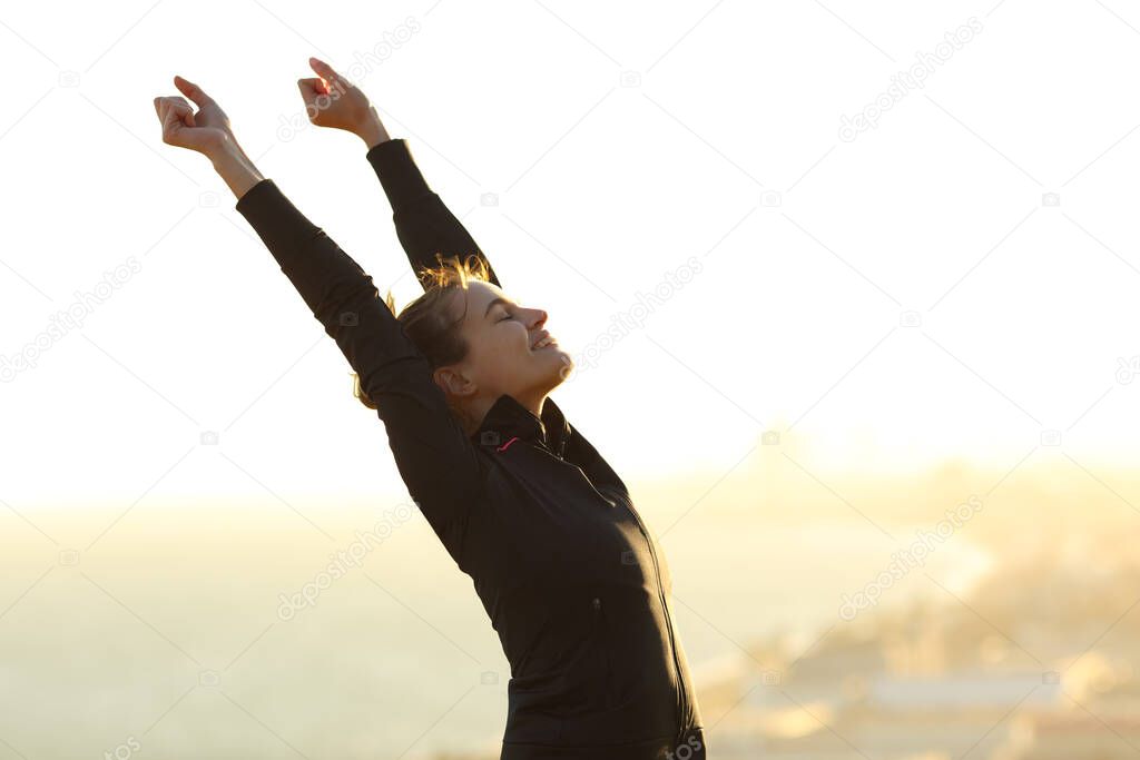 Excited runner raising arms celebrating achievement outdoors at sunset in city outskirts