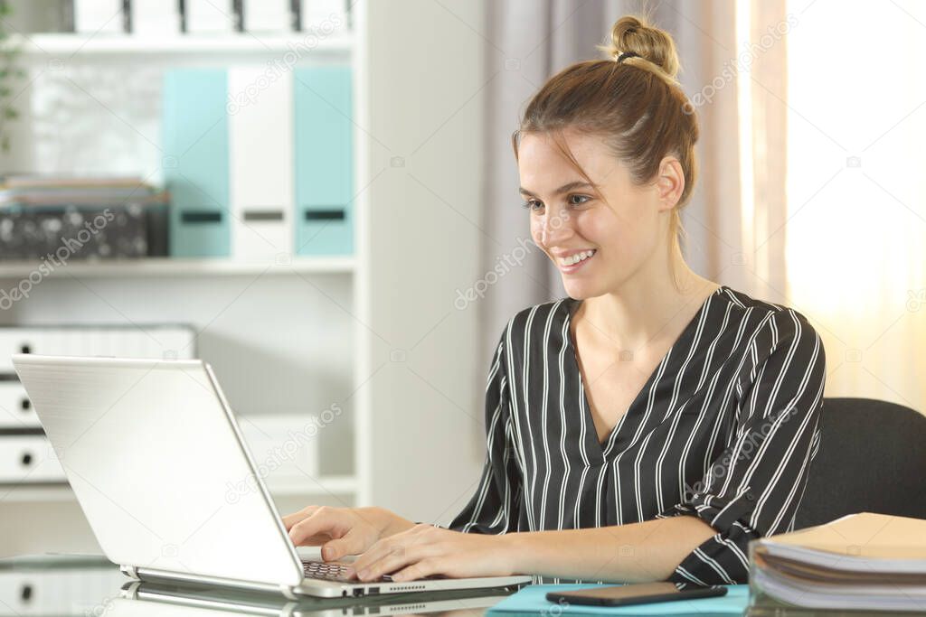 Happy entrepreneur woman using laptop sitting on a desk at home office