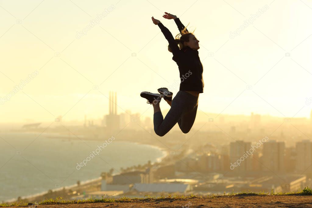 Happy runner jumping celebrating success at sunset in city outskirts