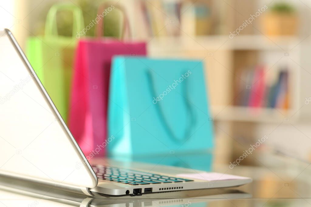 Laptop and colorful shopping bags placed over a desk at home