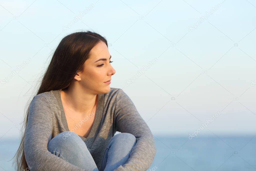 Melancholic woman complaining looking away sitting on the beach