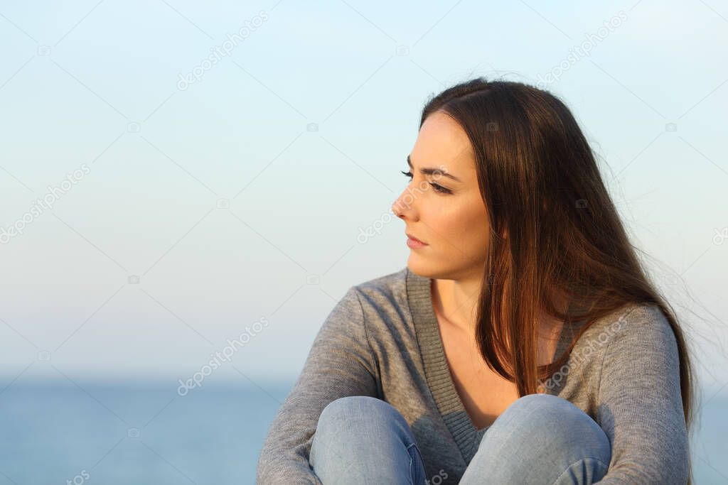 Pensive melancholic woman looking away sitting on the beach at sunset