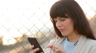 Sokakta duran akıllı telefonu kullanan yetişkin bir kadın.