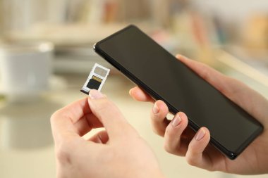Sim ve SD kartını evdeki bir masada oturan akıllı telefona yerleştiren kızın elini kapat.