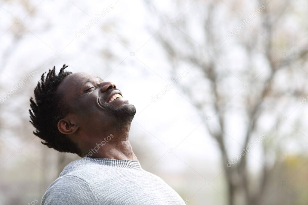 Happy black man breathing fresh air outdoors in winter standing in a park