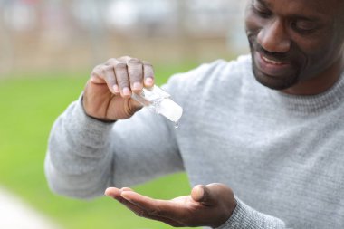Close up of black man using hand sanitizer rub standing in a park clipart