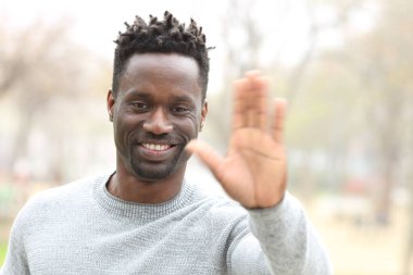 Mutlu siyah adam el sallıyor ve bir parkta kameraya bakıyor.