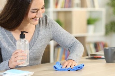 Mutlu kadın dezenfektanla masayı temizliyor ve bulaşıcı hastalıktan korunuyor.