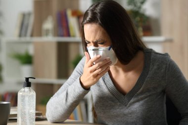 Sick woman coughing with coronavirus symptoms wearing mask sitting on a desk at home in the night clipart