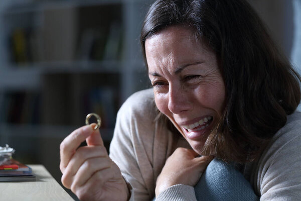Sad wife crying looking at wedding ring sitting in the floor in the night at home