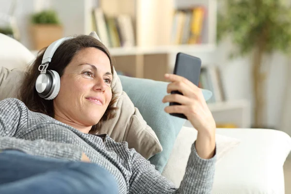 Šťastná Dospělá Dáma Sluchátky Poslouchá Hudbu Chytrém Telefonu Ležící Gauči — Stock fotografie
