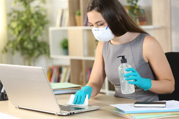 Entrepreneur woman with mask disinfecting computer keyboard with sanitizer and wipe sitting on a desk at homeoffice
