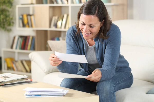 Happy middle age woman looking receipts sitting in the livingroom at home