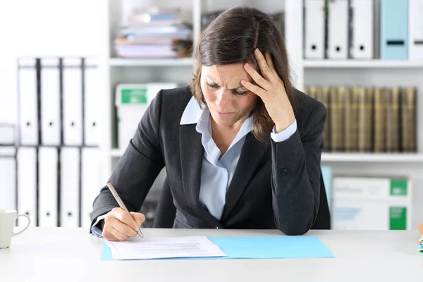 Hesitant adult executive woman doubting signing contract sitting on a desk at the office