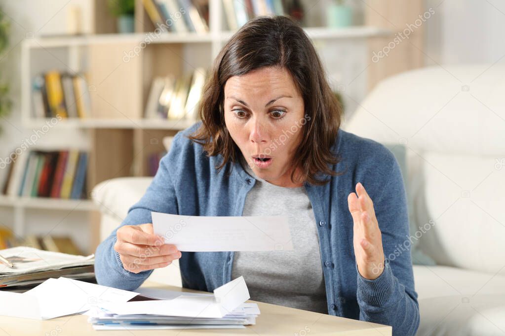 Surprised adult woman checking receipt letters sitting in the livingroom at home