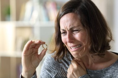 Sad adult wife crying complaining looking at wedding ring sitting at home clipart