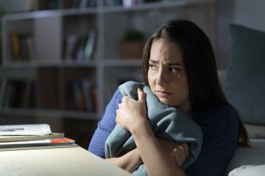 Korkmuş bir kadın gece evde tek başına otururken başka tarafa bakıyor.