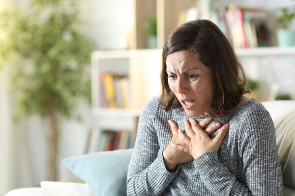 Middle age woman wheezing touching chest sitting on a couch at home
