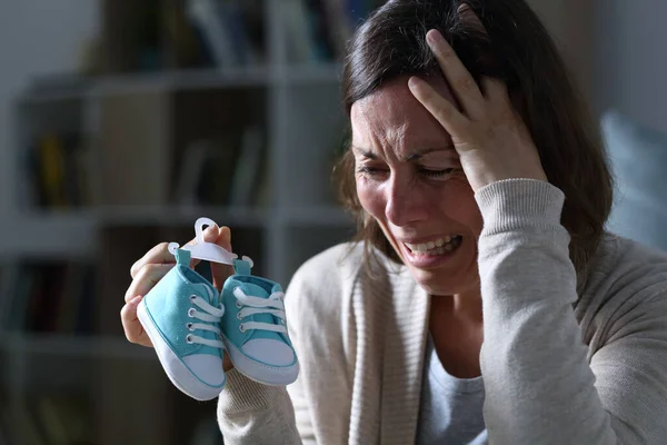 Üzgün anne çocuğunu kaybettiği için ağlıyor. Düşük yaptıktan sonra evde yeni bir bebek ayakkabısı tutuyor.