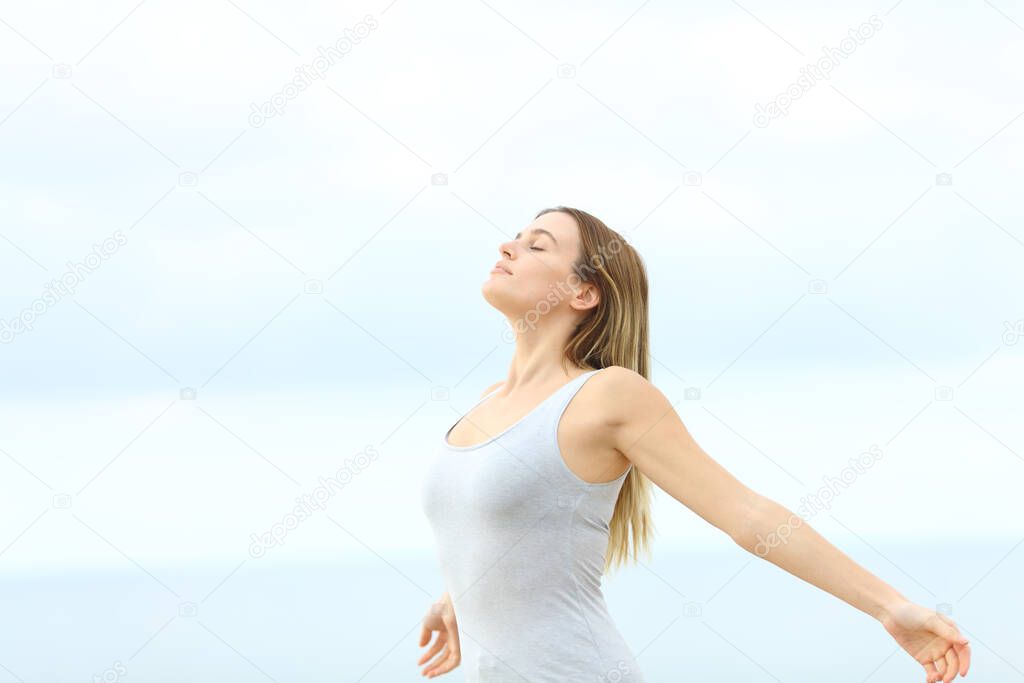 Woman breathing fresh air outstretching arms standing at the beach