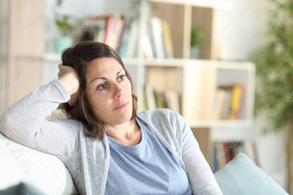 Pensive adult woman thinking looking away sitting on the couch at home